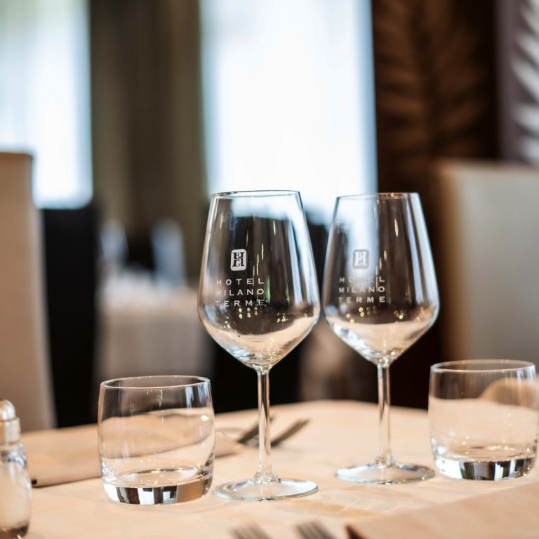 Calici da vino Hotel Milano Terme su tavola elegante del ristorante, mise en place raffinata con bicchieri e posate.