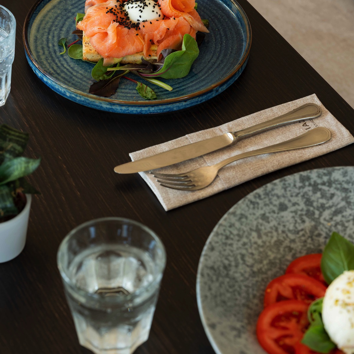 Brunch gourmet: waffle con salmone affumicato, uovo in camicia e insalata, con caprese e bicchiere d’acqua sul tavolo