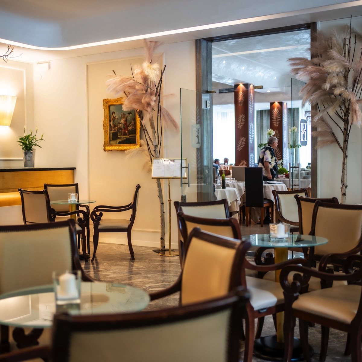 Elegante sala ristorante d'hotel con tavoli in vetro, sedie in legno imbottite, luci soffuse e decorazioni con pampas.