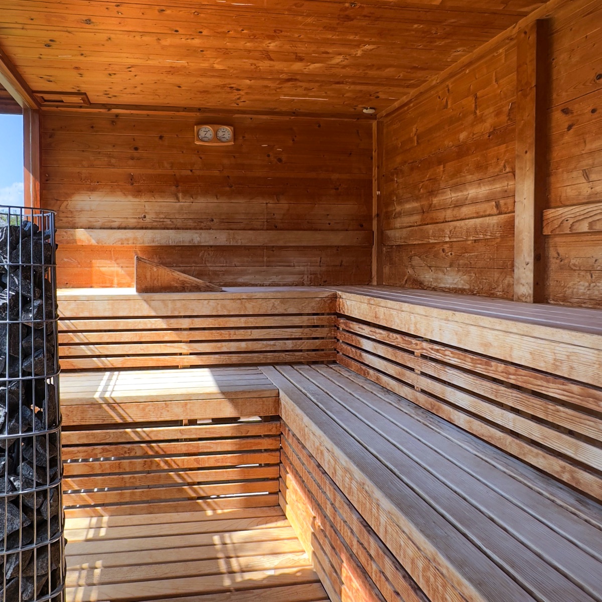 Interno sauna finlandese in legno con panche a gradoni e stufa a pietre, luce naturale, spa benessere e relax