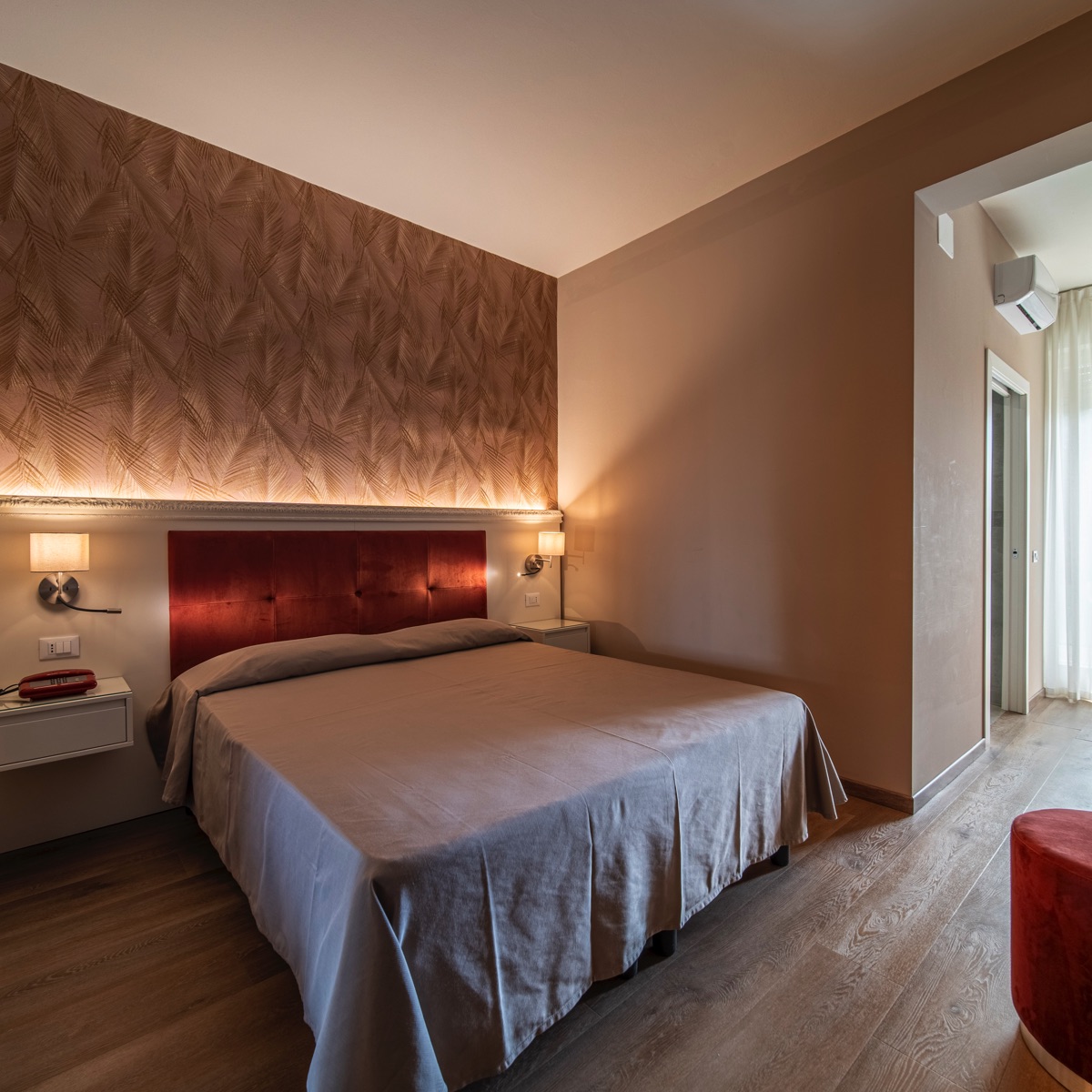 Camera matrimoniale moderna con testiera in velluto rosso, carta da parati dorata, luci LED soffuse e parquet