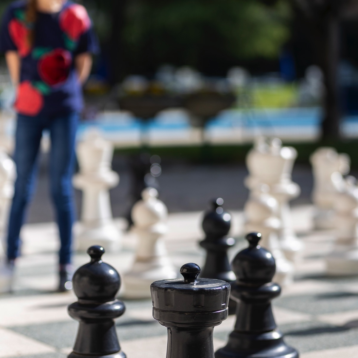 Scacchi giganti all’aperto con re nero in primo piano e persona sfocata pronta a muovere sulla scacchiera