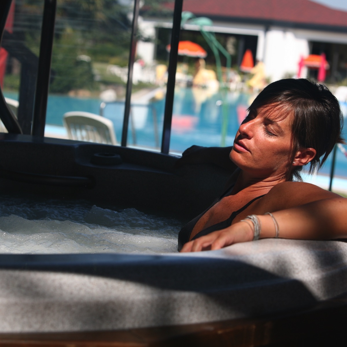Donna che si rilassa in una vasca idromassaggio in spa con piscina all’aperto, sole e atmosfera di benessere in hotel.