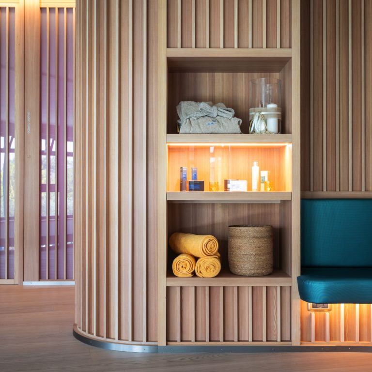 Scaffale spa in legno con accappatoio, prodotti skincare, asciugamani gialli e panca turchese, luce calda wellness.