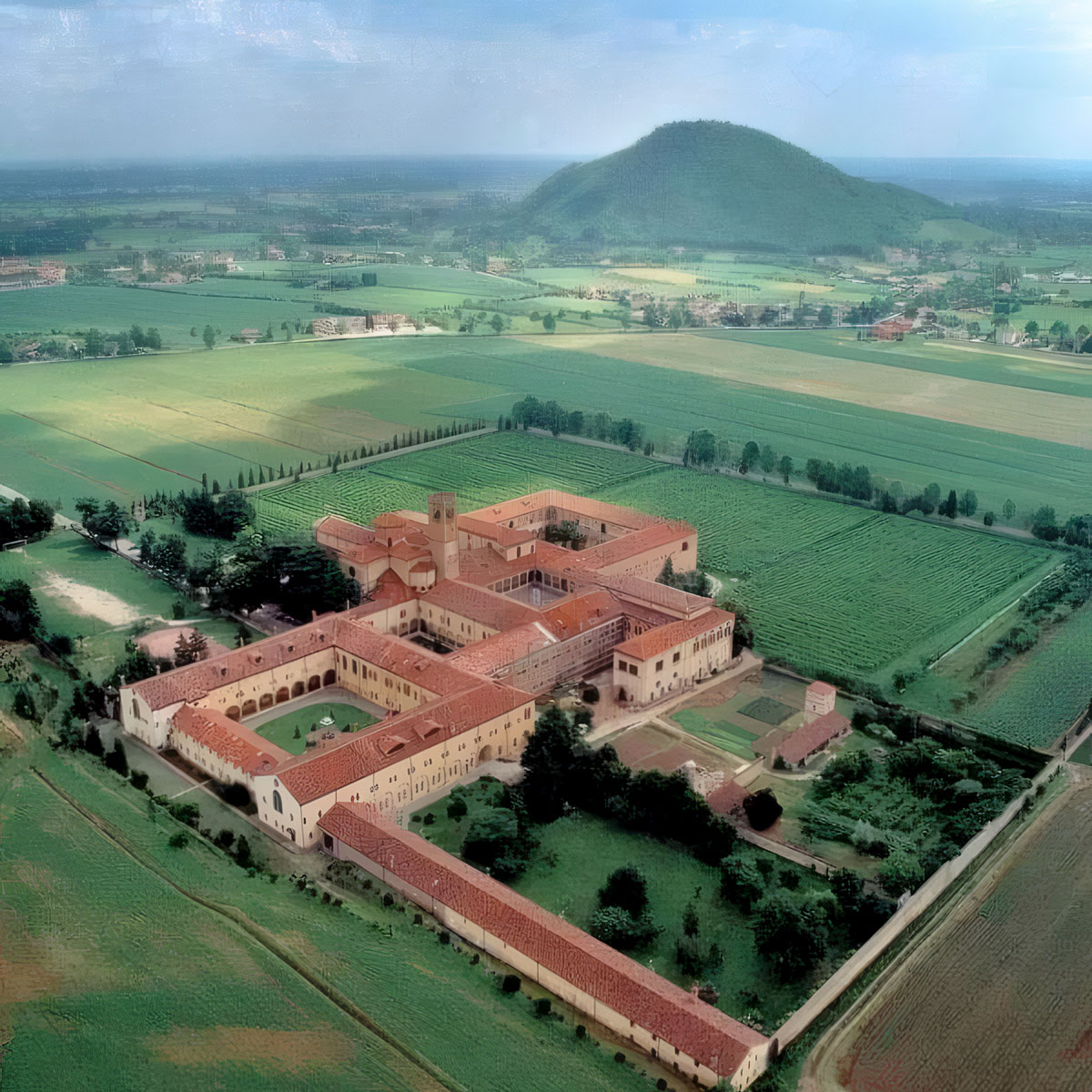 Vista aerea di un grande monastero con chiostri e tetti rossi tra campi verdi, ai piedi dei Colli Euganei, Veneto