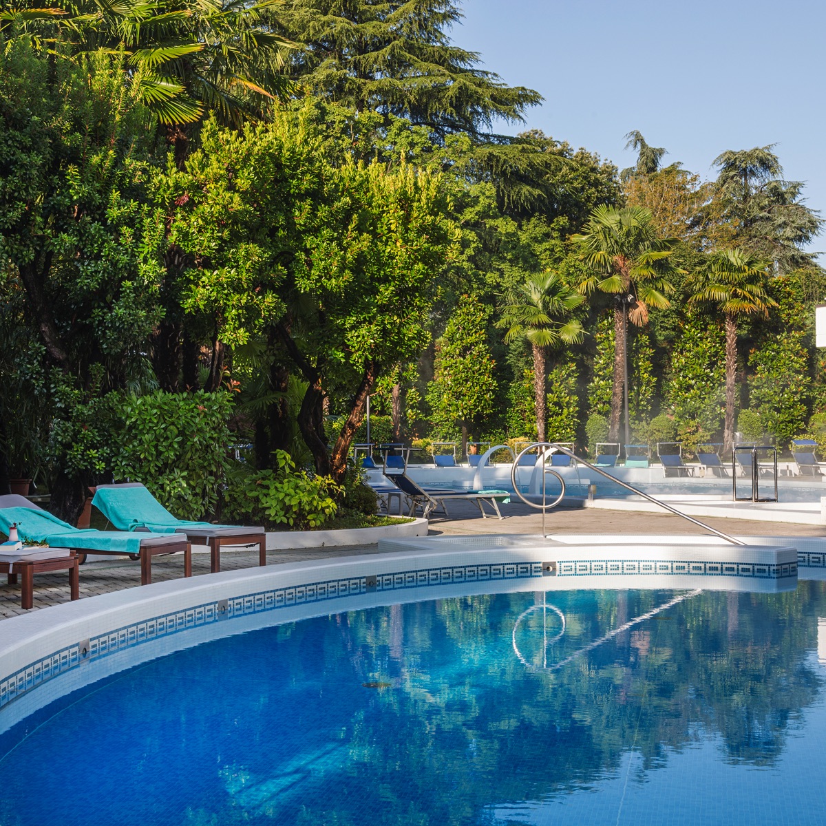 Piscina all'aperto di resort con spa, acqua cristallina, lettini e palme in rigoglioso giardino tropicale, relax al sole.