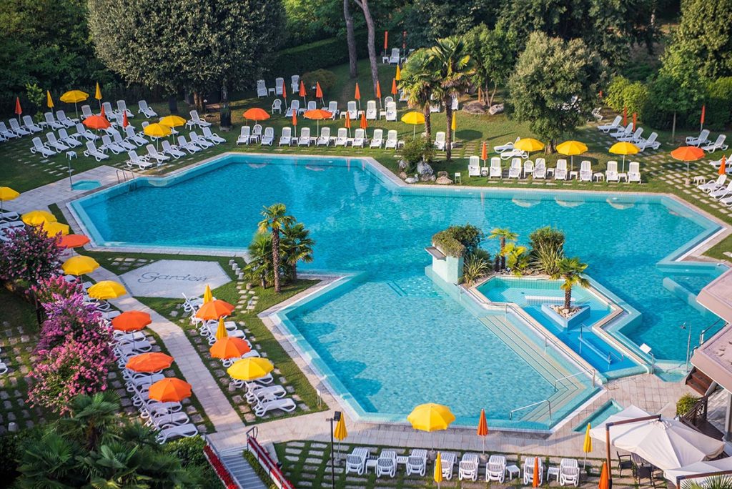 Piscine all’aperto del resort con isole verdi, lettini bianchi e ombrelloni gialli e arancioni