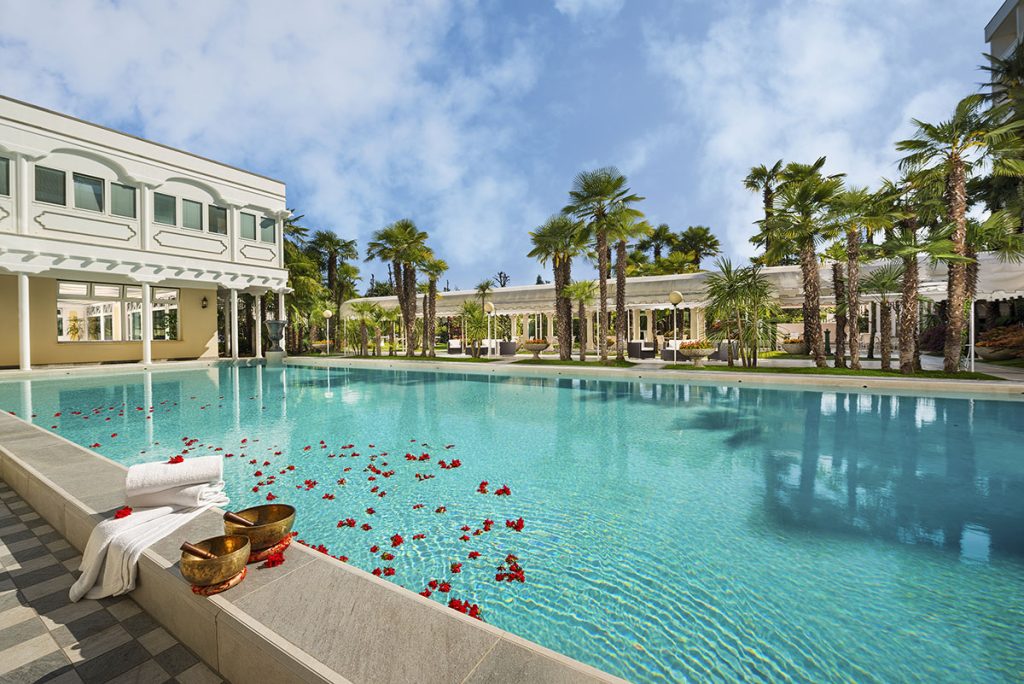 Piscina esterna di hotel spa di lusso con palme, petali di rosa sull’acqua, asciugamani e ciotole benessere, relax al resort.