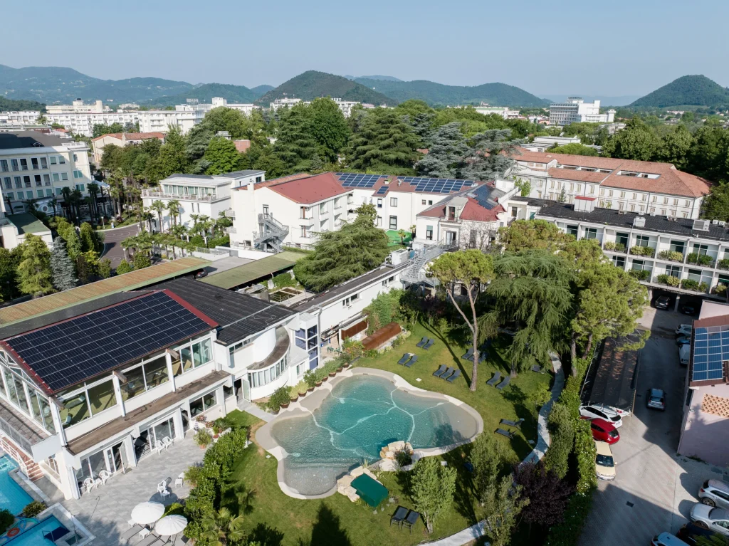 Veduta aerea di resort termale con piscina laguna, giardino e pannelli solari, circondato da colline verdi.