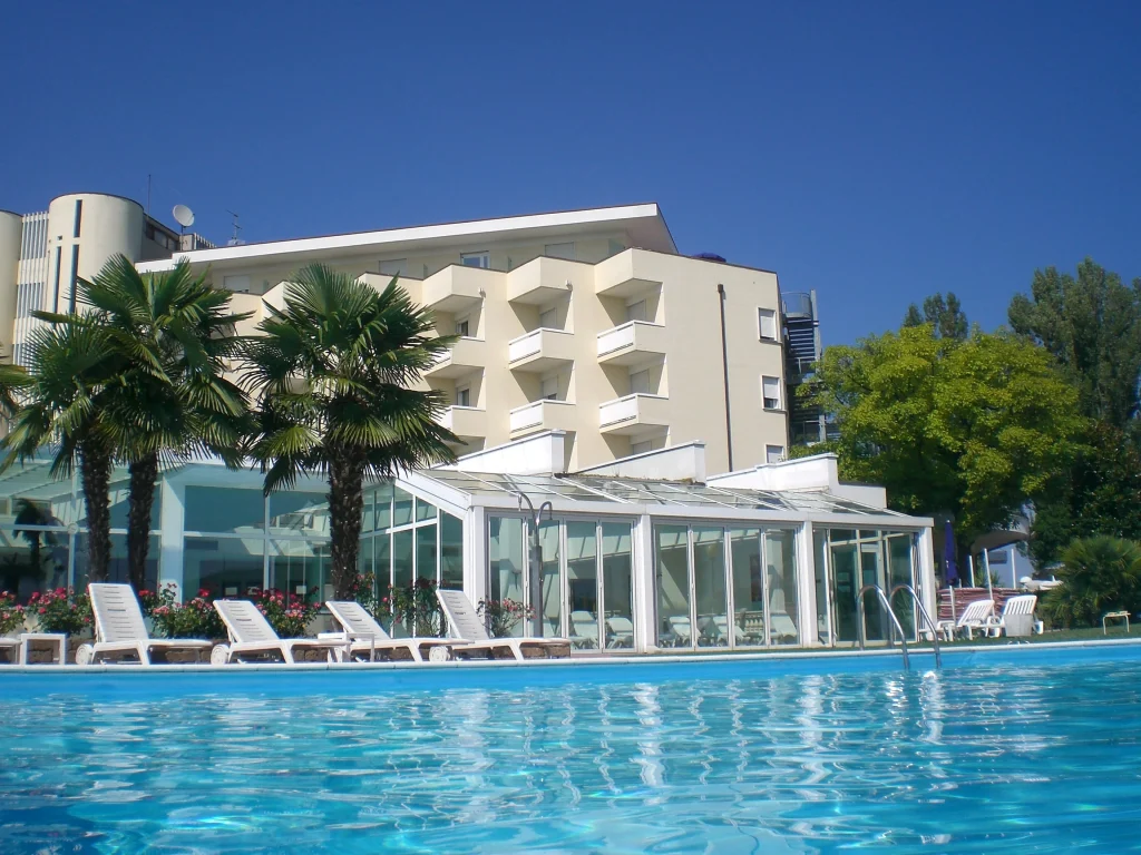 Resort hotel con ampia piscina esterna, lettini e palme, sotto cielo blu: destinazione relax per vacanze estive.